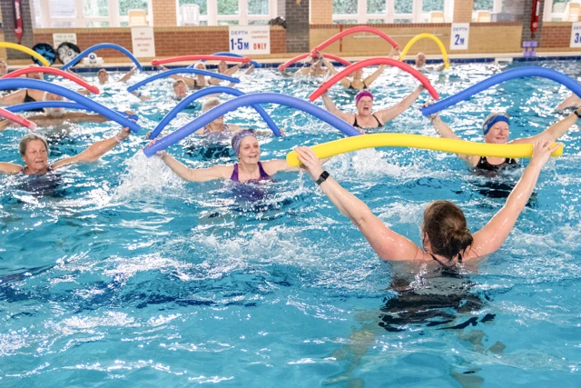 Aqua Aerobics Aqua Mobility class instructor leads participants exercising with dumbbells in a pool.