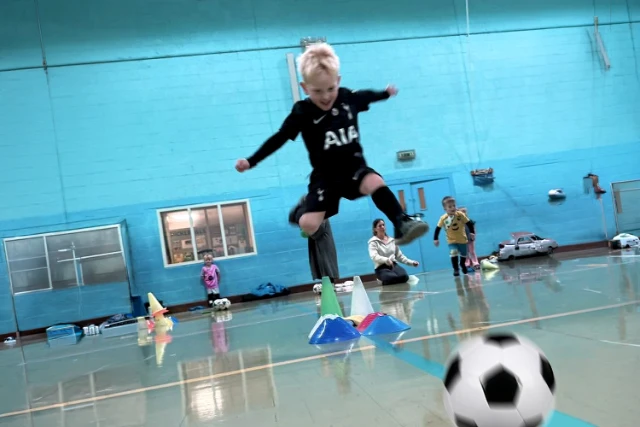 Tots Football A young child jumps and kicks a ball at tots football