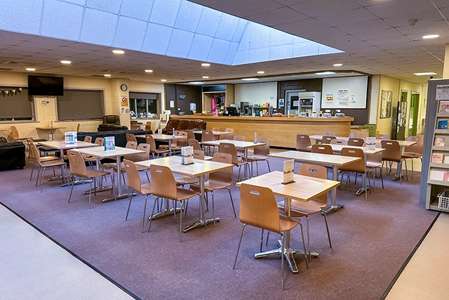 Cafe This image shows an empty cafe dining area with tables and chairs. A counter with kitchen equipment is visible in the background.