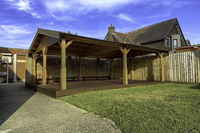 Garden canopy The Garden Canopy, a wooden outdoor shelter with a raised deck stands in a yard next to a brick building and a wooden fence. The sky above is blue with wispy white clouds.