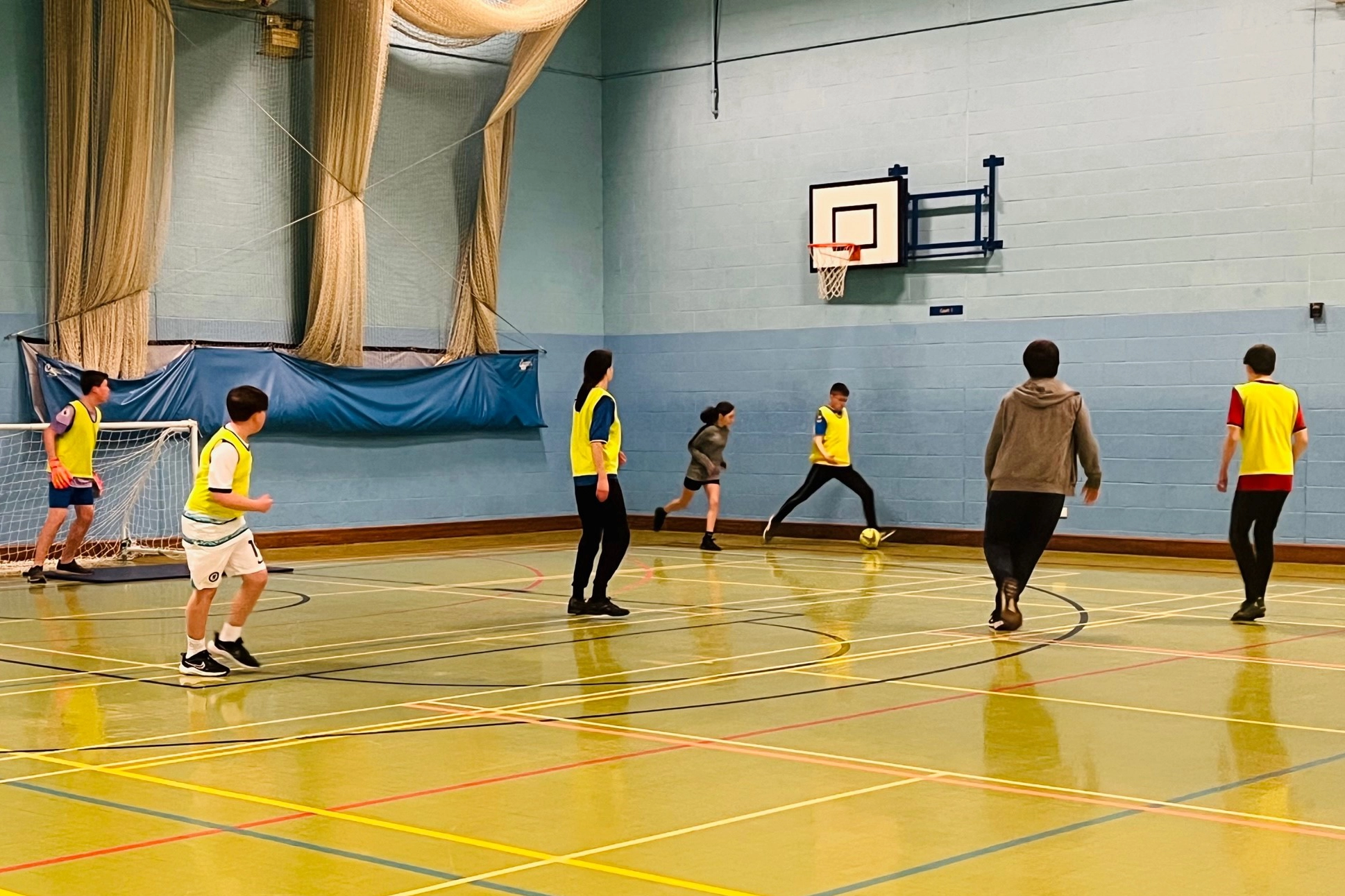 Youth Football A group of young people are playing football in the sports hall. They are wearing brightly colored vests over their athletic clothing.